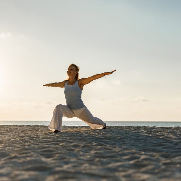 Young woman doing Yoga balance exercises with her arms outstretched on the beach at sunrise. Copy space.